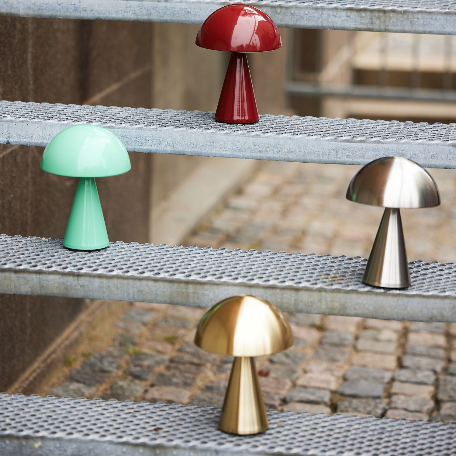 Vier tragbare Lampen in rot, grün, nickel und messing auf einer Metaltreppe