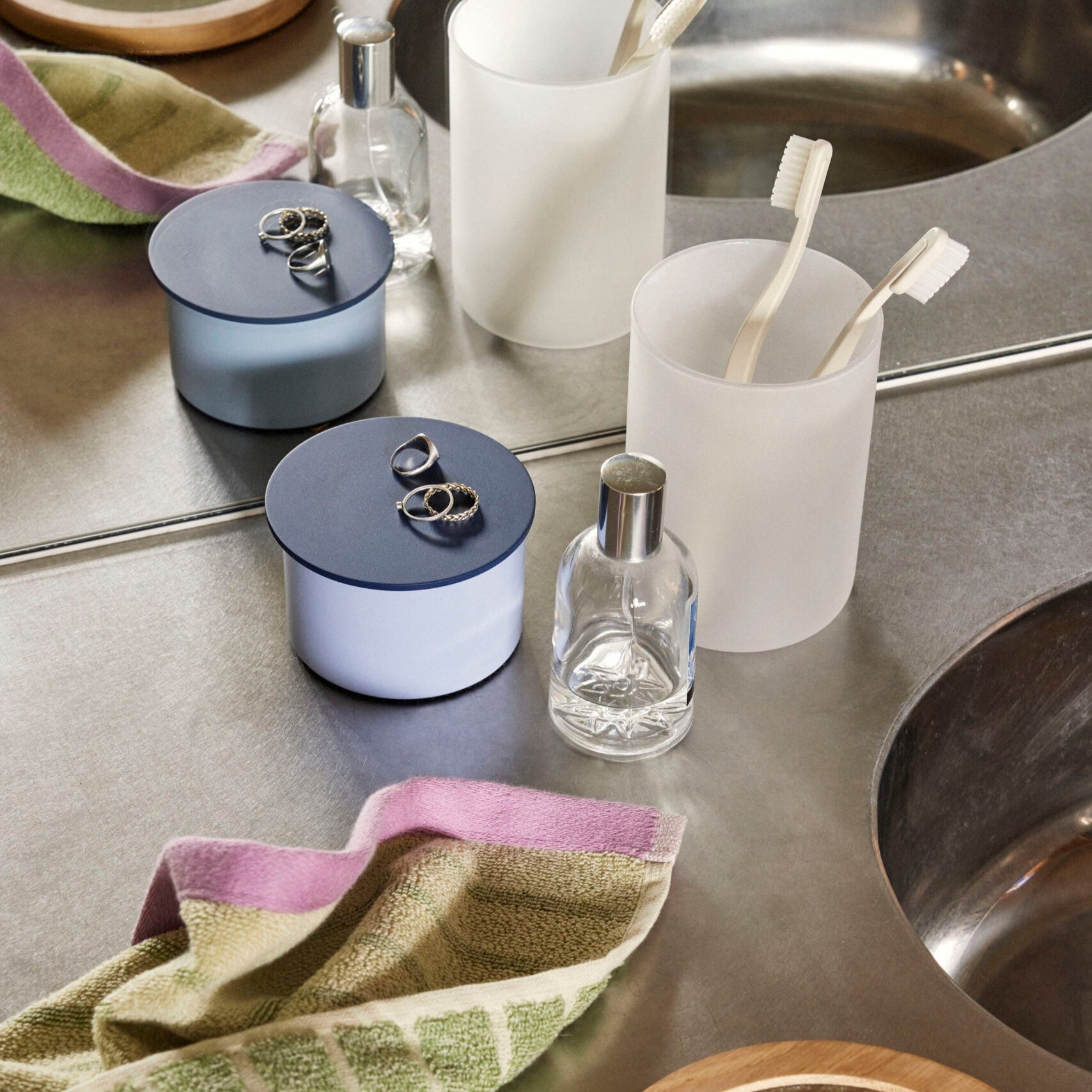 Aufbewahrungsbox und Zahnputzbecher auf Waschbecken vor einem Spiegel