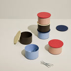 Sechs kleine bunte Metaldosen auf einem Tisch mit Büroklammern dekoriert