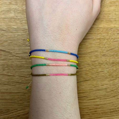 Ein Handgelenk auf dem vier verschieden farbige Inca Armbänder zu sehen sind.