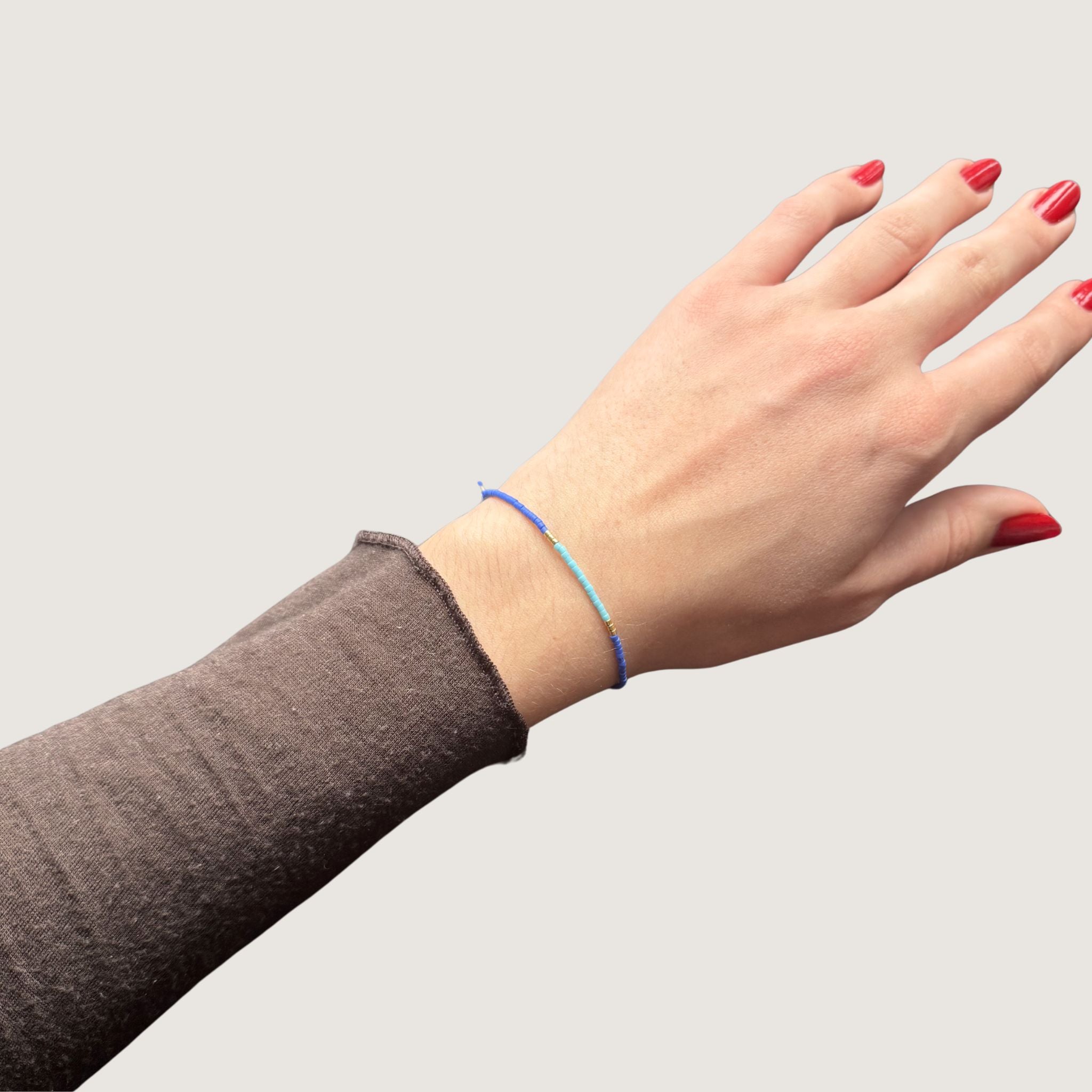Zweifarbiges Perlenarmband in blau und hellblau getrennt duch jeweils drei goldene Perlen. Gezeigt an einem Handgelenk.