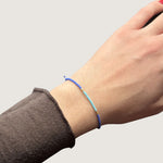 Zweifarbiges Perlenarmband in blau und hellblau getrennt durch jeweils drei goldene Perlen. Gezeigt an einem Handgelenk.