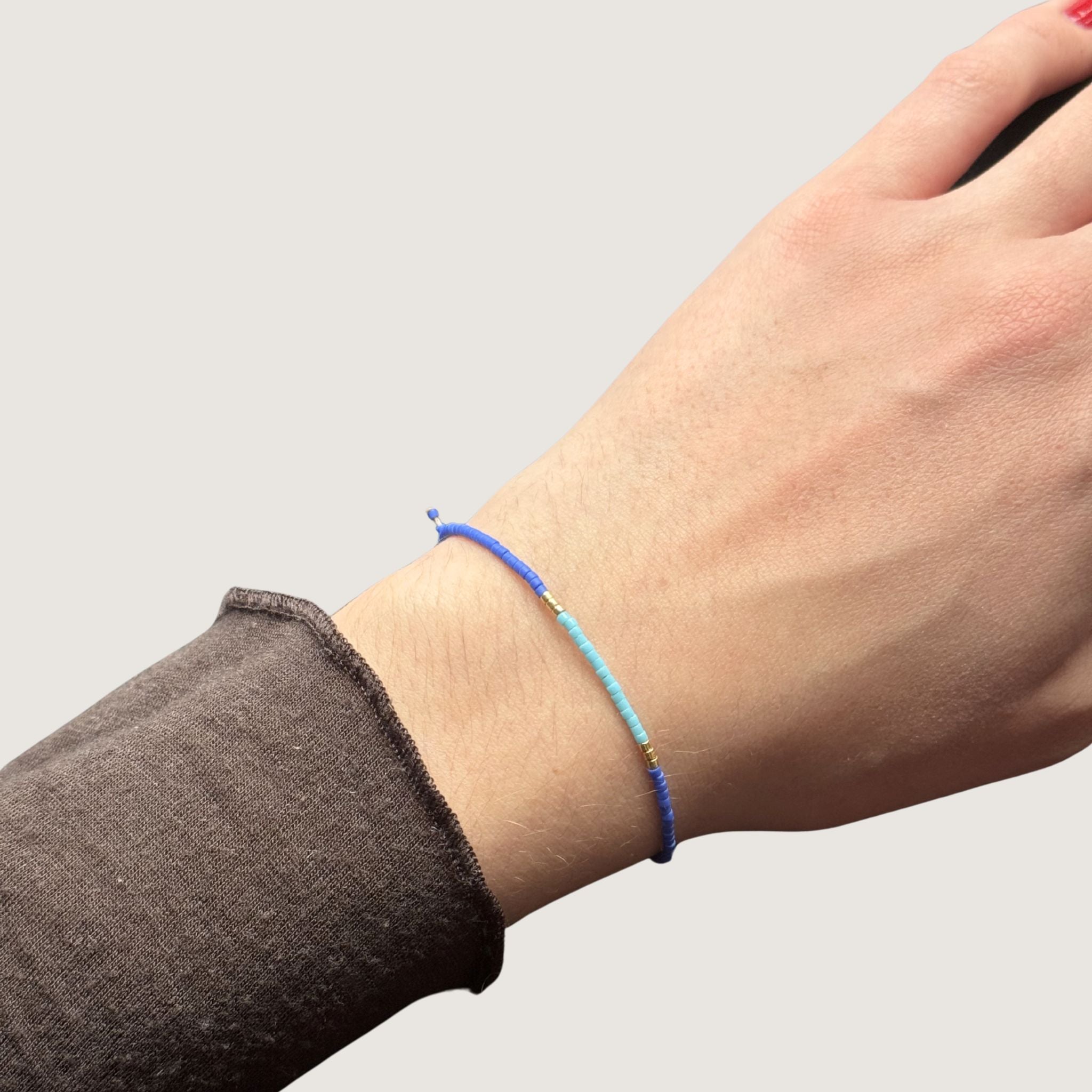 Zweifarbiges Perlenarmband in blau und hellblau getrennt durch jeweils drei goldene Perlen. Gezeigt an einem Handgelenk.