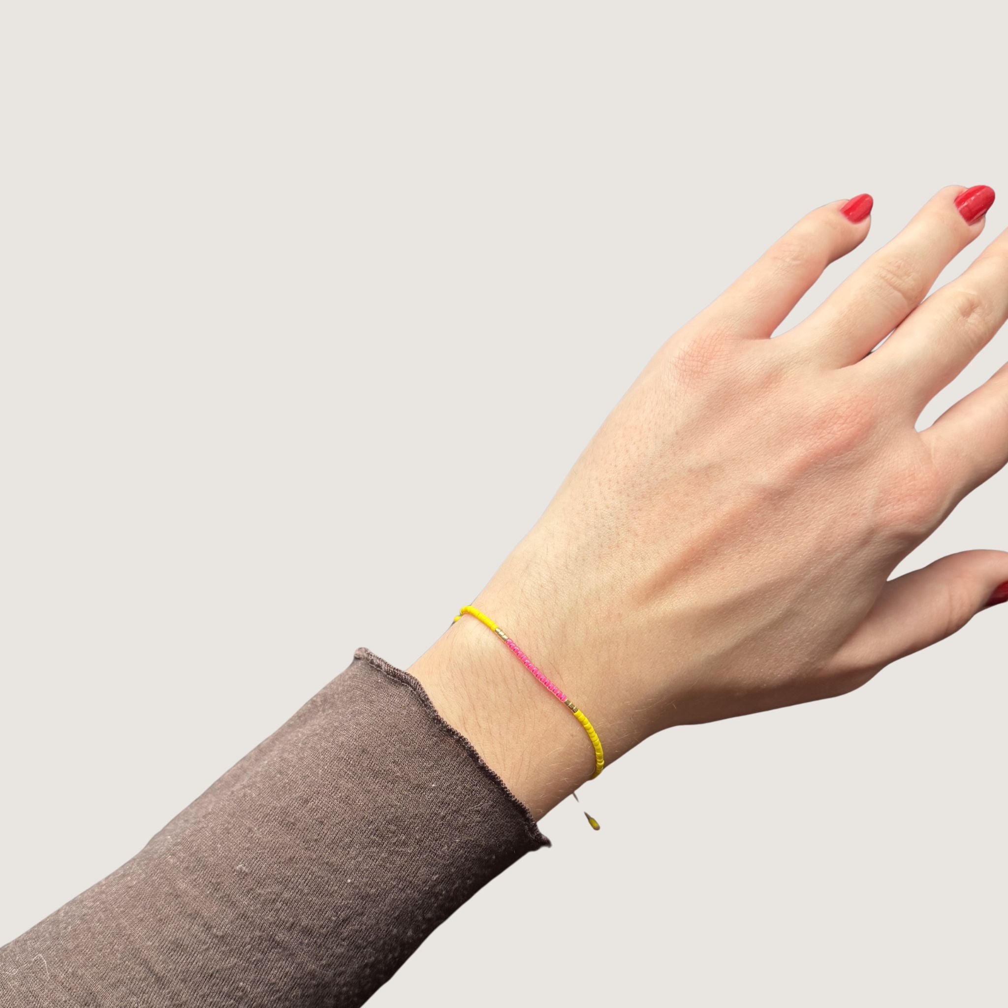 Zweifarbiges Perlenarmband in gelb und pink getrennt durch jeweils drei goldene Perlen. Gezeigt an einem Handgelenk.