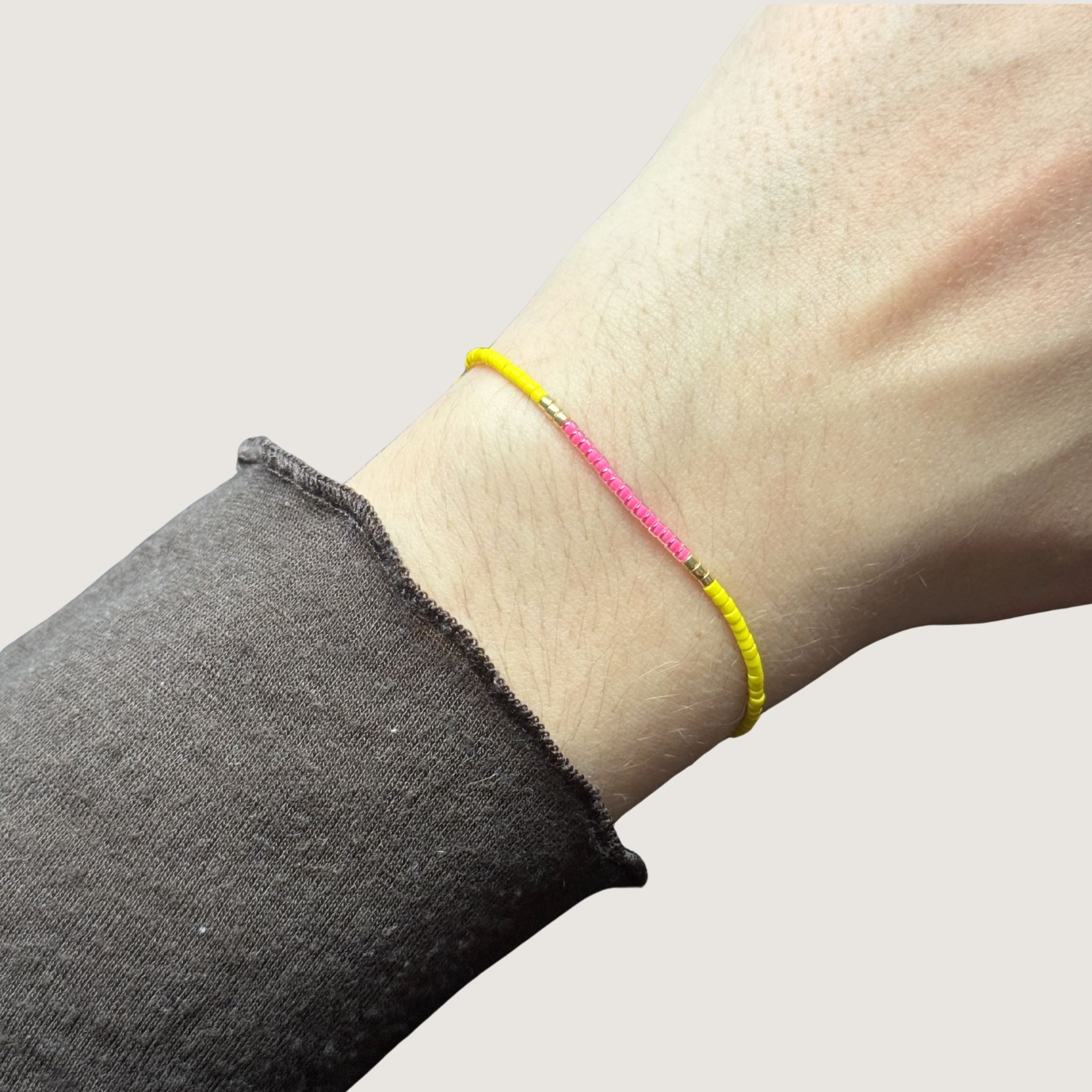 Zweifarbiges Perlenarmband in gelb und pink getrennt durch jeweils drei goldene Perlen. Gezeigt an einem Handgelenk.