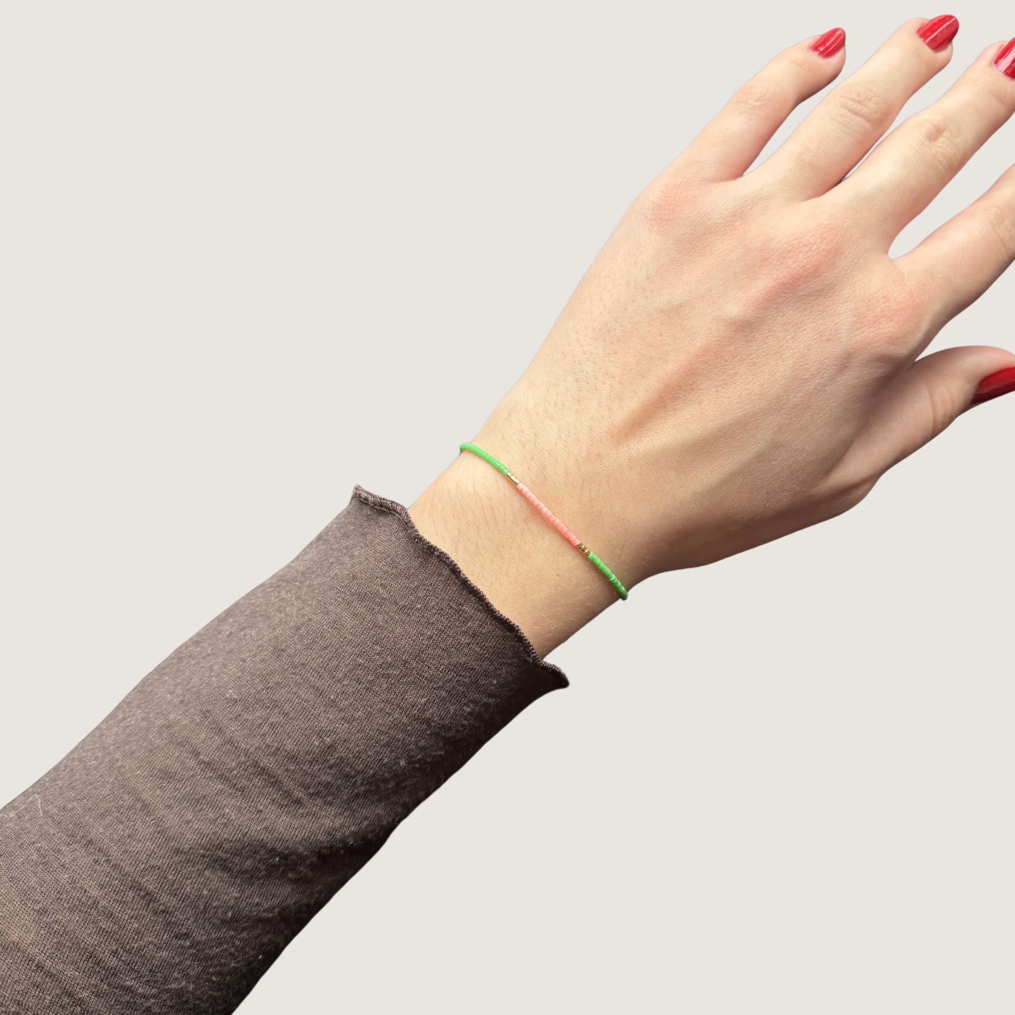 Zweifarbiges Perlenarmband in hellgrün und hellrosa getrennt durch jeweils drei goldene Perlen. Gezeigt an einem Handgelenk.
