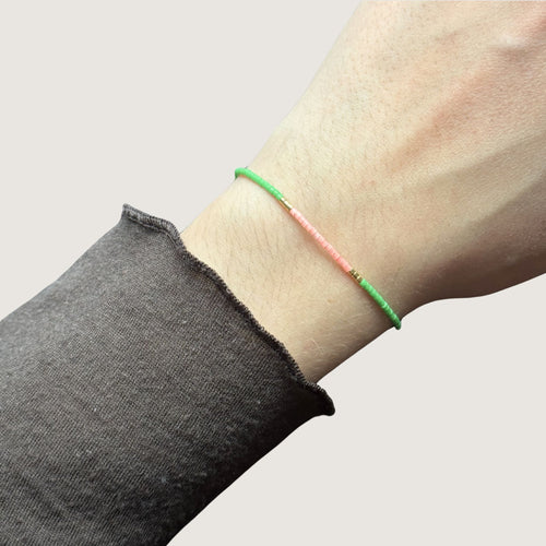 Zweifarbiges Perlenarmband in hellgrün und hellrosa getrennt durch jeweils drei goldene Perlen. Gezeigt an einem Handgelenk.