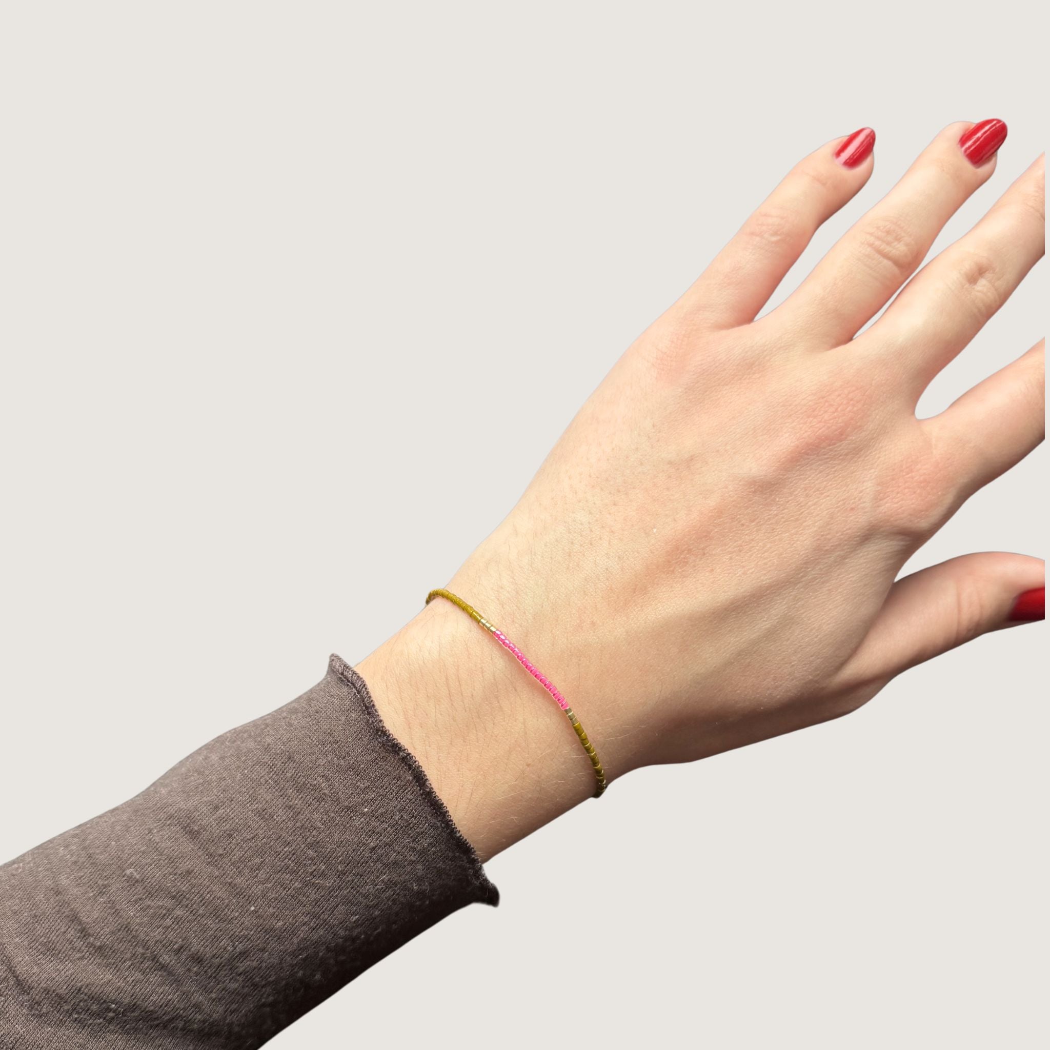 Zweifarbiges Perlenarmband in olivgruen und pink getrennt durch jeweils drei goldene Perlen. Gezeigt an einem Handgelenk.
