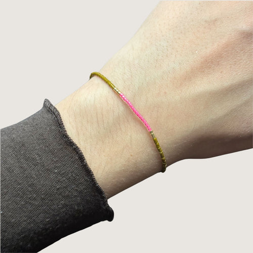Zweifarbiges Perlenarmband in gelb und pink getrennt durch jeweils drei goldene Perlen. Gezeigt an einem Handgelenk.