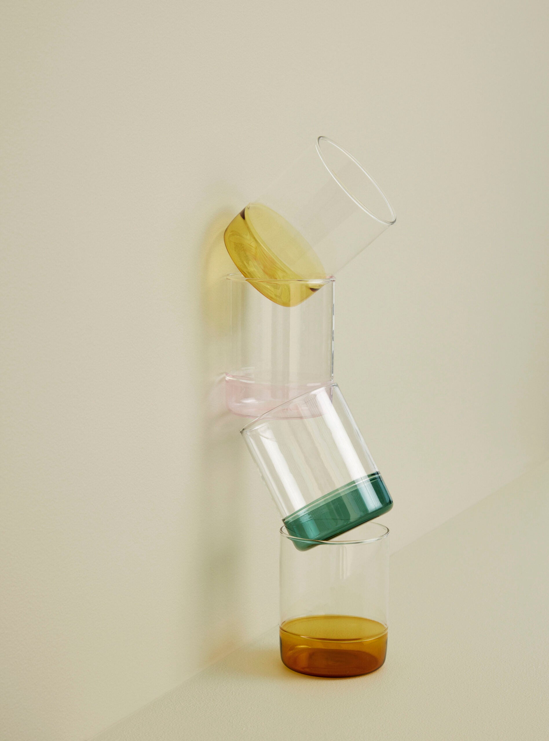 glas mit gelbem boden im stapel mit anderen farbigen gläsern an wand gelehnt