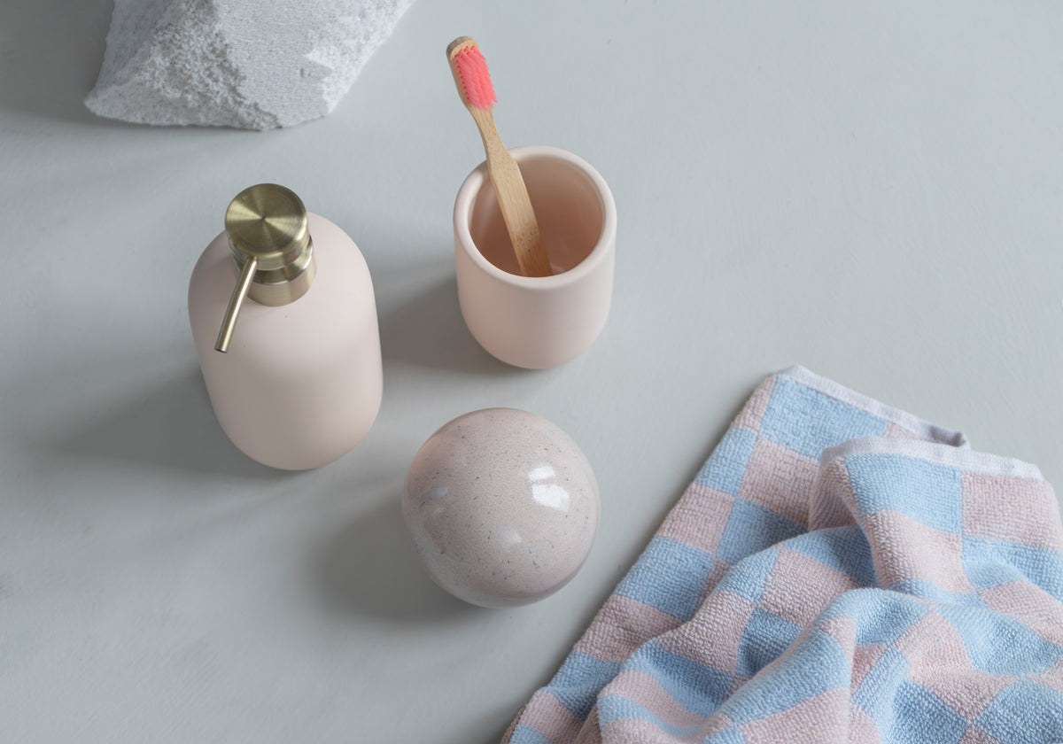 Badezimmeraccessoires in rosa mit karriertem Handtuch.