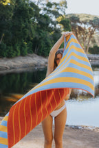 frau schwingt gelb und blau gestreiftes badetuch aus bio-baumwolle am seeufer