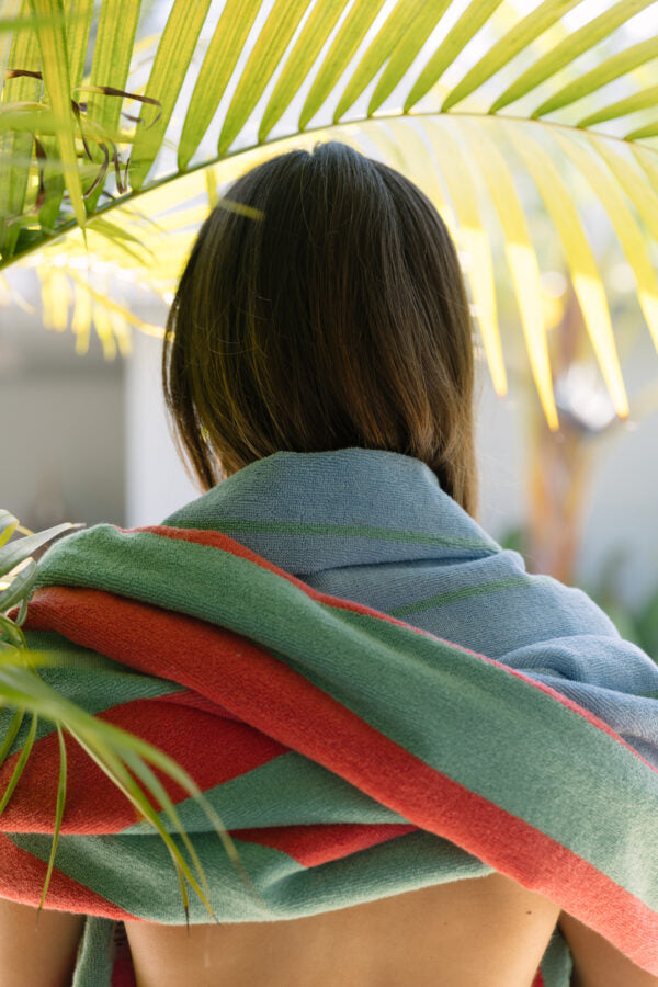 frau mit grün gestreiftem badetuch aus bio-baumwolle über den schultern unter palmen