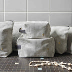 gestreifte kosmetiktaschen in würfelform aus bio-baumwolle auf schwarz-weißem fliesenboden vor weißer kachelwand