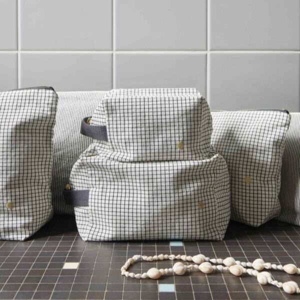 gestreifte kosmetiktaschen in würfelform aus bio-baumwolle auf schwarz-weißem fliesenboden vor weißer kachelwand