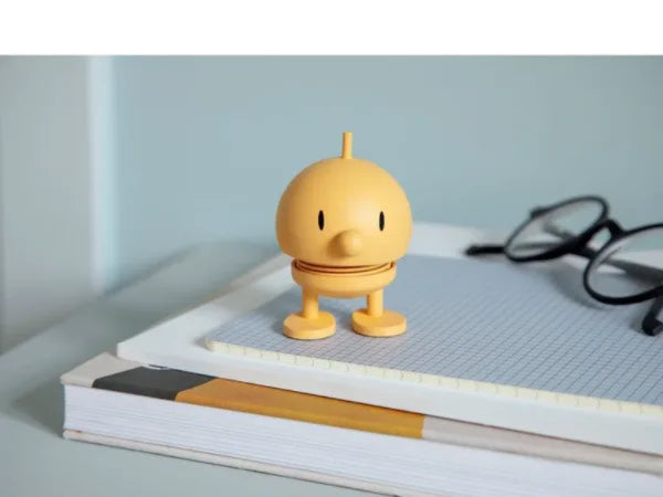 hoptimist figur bumble soft mimosa gelb auf einem heft auf einem schreibtisch