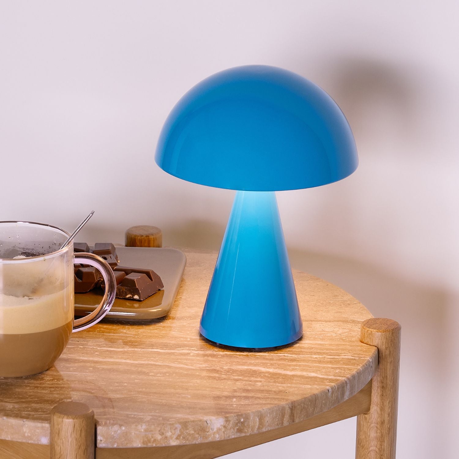 Tragbare Lampe in blau auf Holztisch mit Kaffee und Schockolade