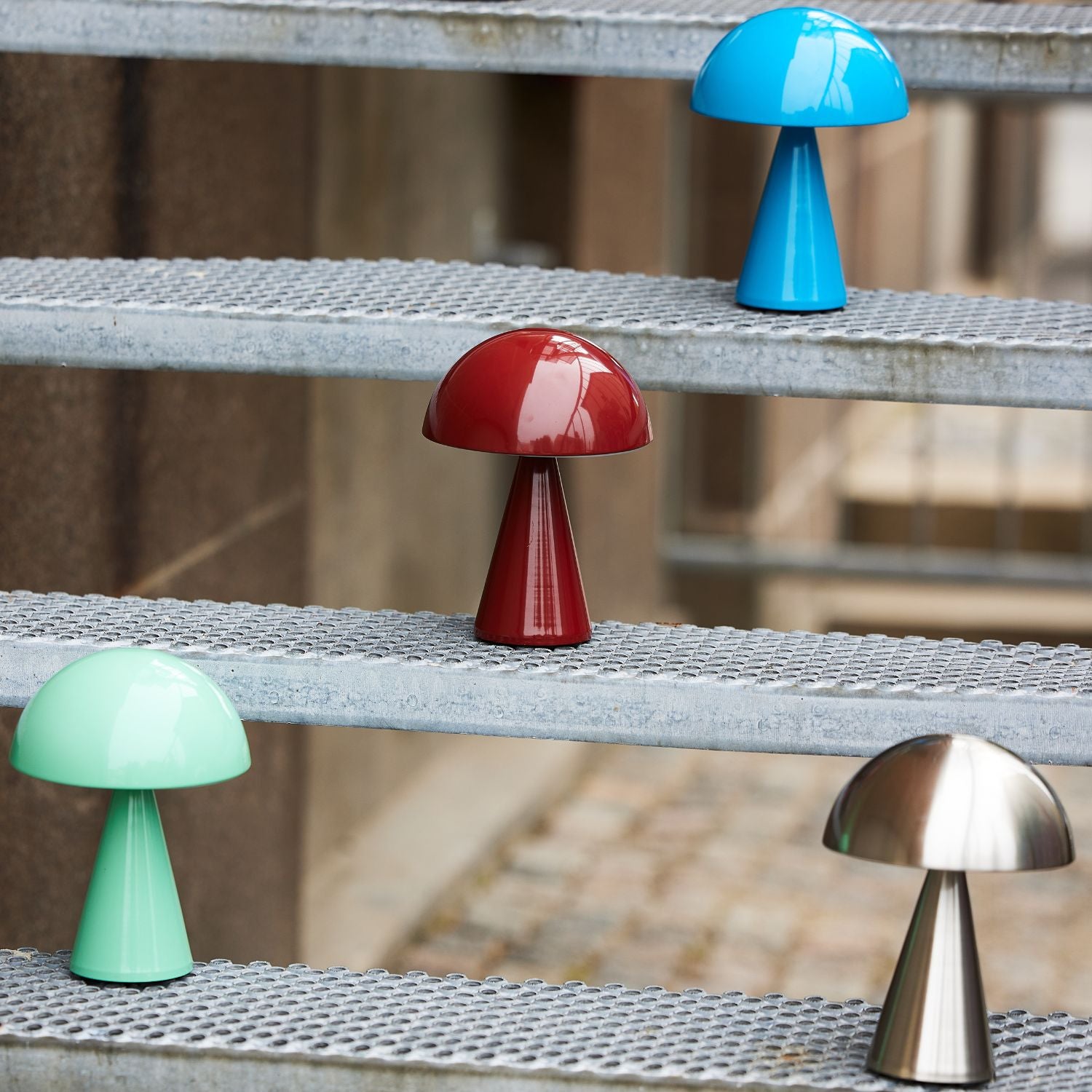Vier tragbare Mush Lampen von Huebsch in rot, blau, grün und messing auf einer Metaltreppe.