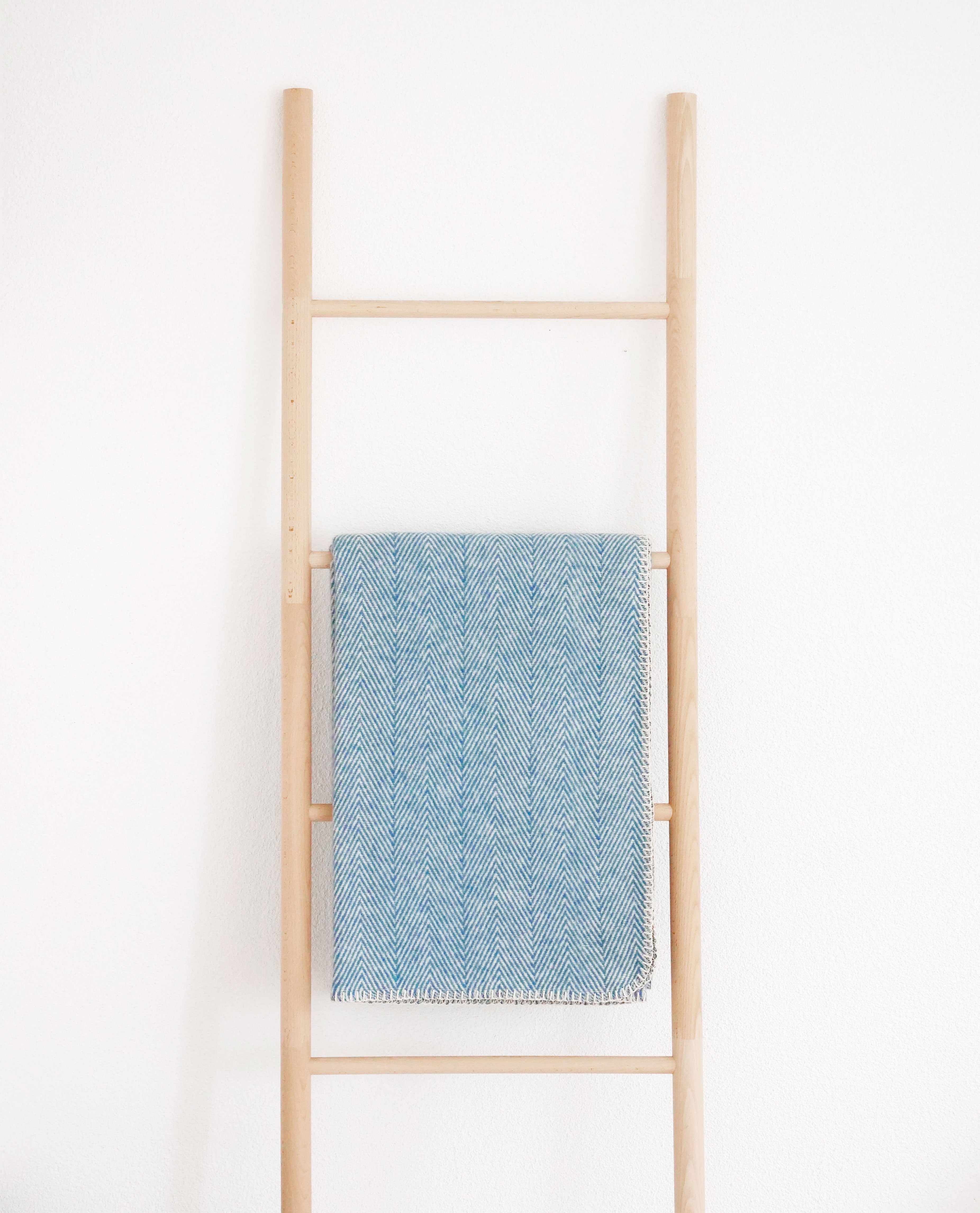 baumwolldecke in blau mit fischgrätmuster über holzleiter vor weißer wand