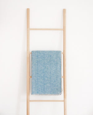 baumwolldecke in blau mit fischgrätmuster über holzleiter vor weißer wand