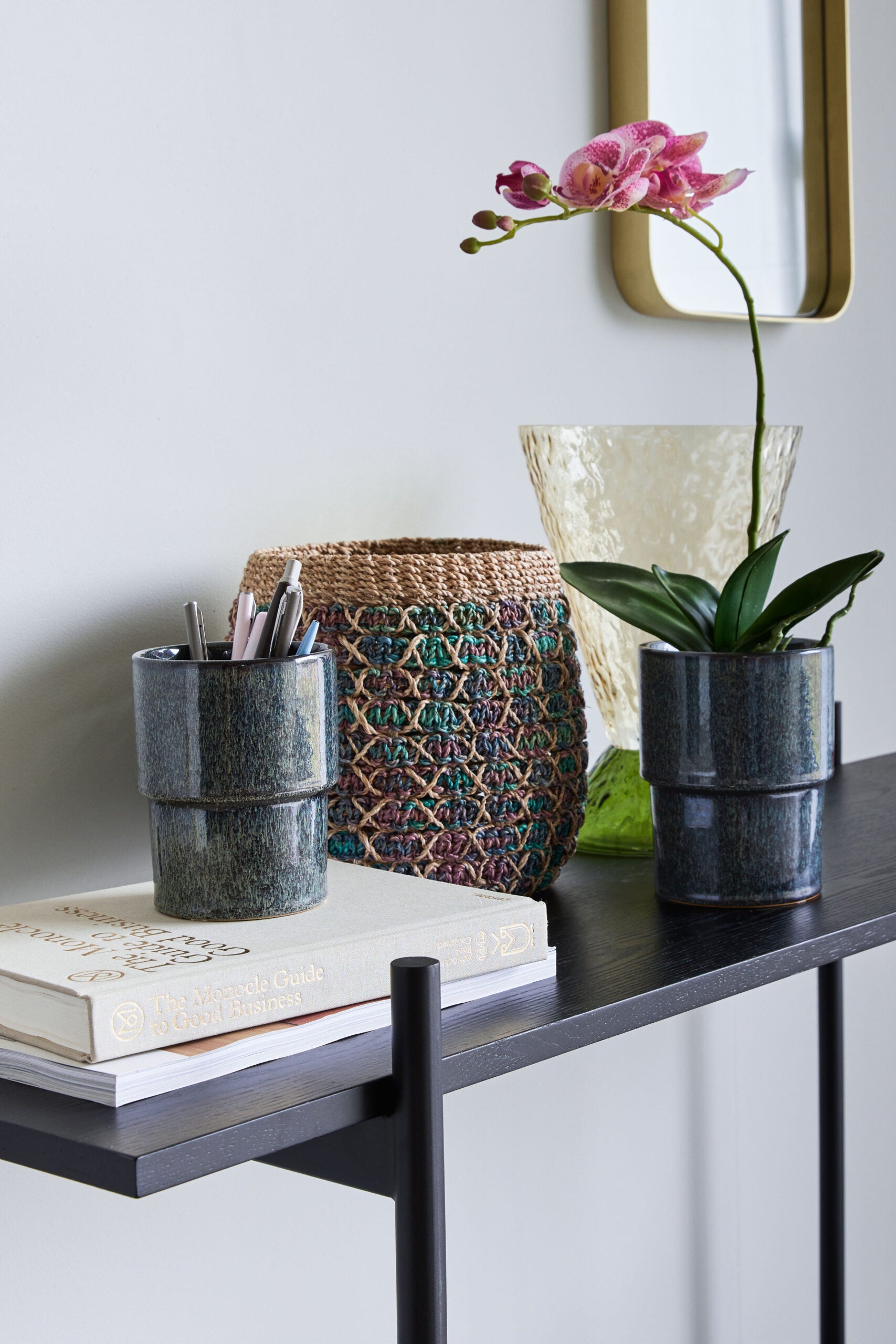 zwei dunkelgrüne keramikübertöpfe mit glasierter oberfläche als stiftehalter und pflanzgefäss auf schwarzem schreibtisch