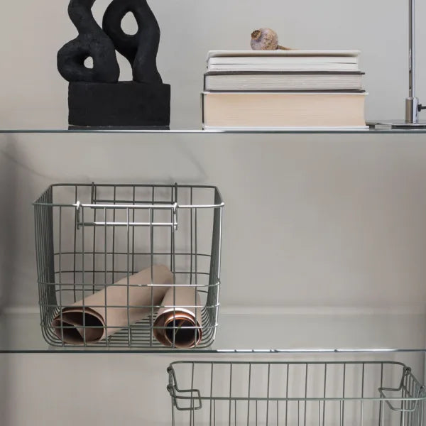 gruener drahtkorb in einem glasregal mit verschiedenen dekoobjekten