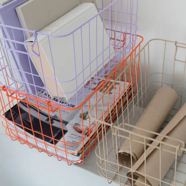 nahaufnahme von drei drahtkörben in sand orange und lila mit zeitschriften und buechern als büro oder wohnaccessoire