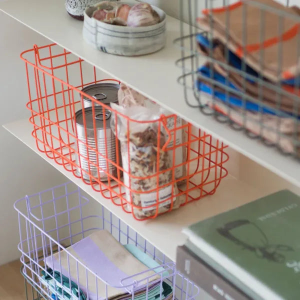 drei drahtkoerbe in gruen orange und lila dekoriert in einem regal