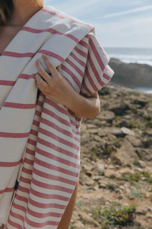 Frau mit Torres Novas Barra Strandtuch in Rot-Weiß gestreift an Felsküste hochwertiges Hamamtuch aus Portugal